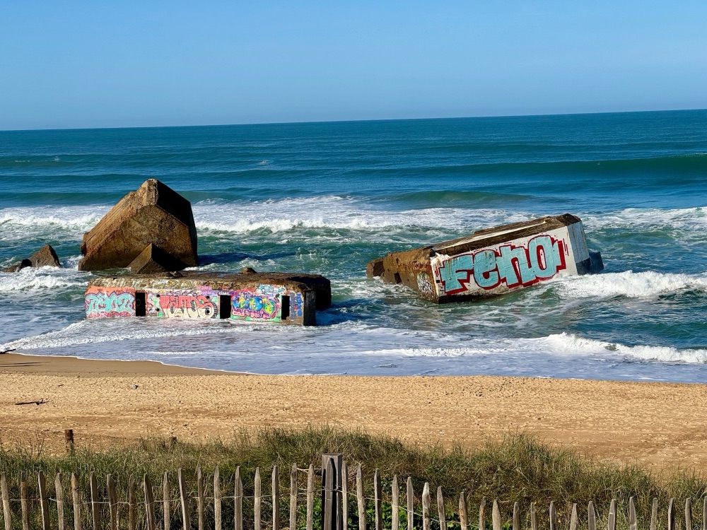 Graffiti-covered wartime bunkers lying in the surf on a wide Atlantic beach