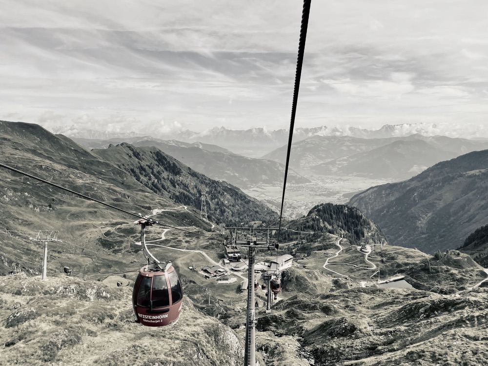 A cable car descending into a wide mountain valley, in near-monochrome