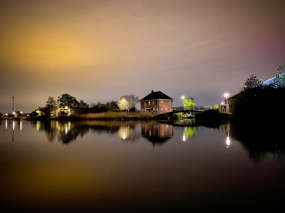 A house by the water at dusk, its lights reflected in the still surface