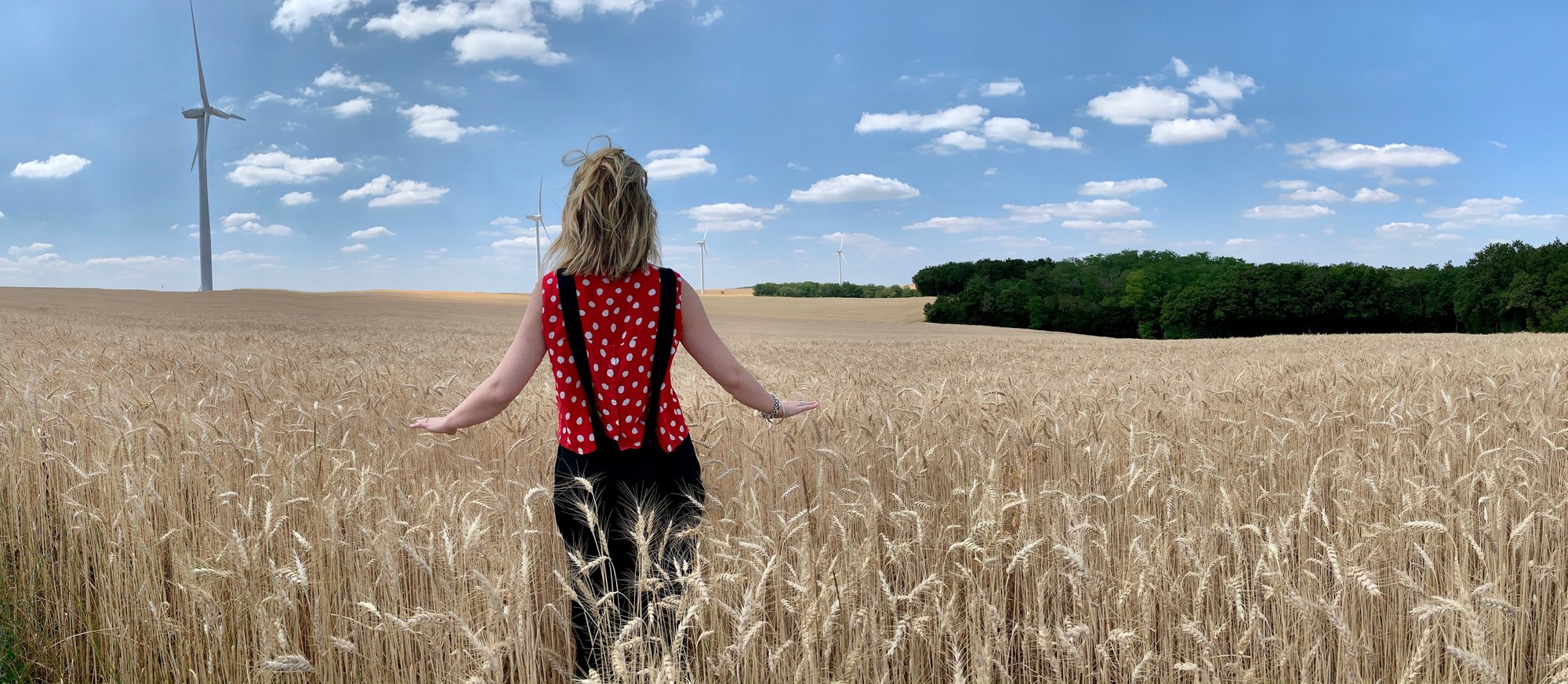 A woman walking into a ripening wheat field under a wide sky